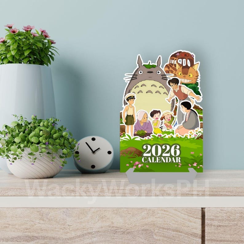 May include: A 2026 calendar featuring characters from a popular animated film. The calendar has a green base with the text "2026 CALENDAR". The characters are set against a backdrop of a green field and blue sky. The calendar is on a wooden surface.