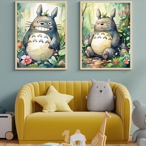 May include: Two framed watercolor prints of the character Totoro from the animated film My Neighbor Totoro. The prints feature the character in a forest setting. The prints are displayed above a yellow sofa with decorative pillows.