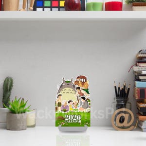May include: A 2026 calendar featuring a cartoon image of a large, gray Totoro character with other animated characters. The calendar has a green and white base with the text "2026 CALENDAR".