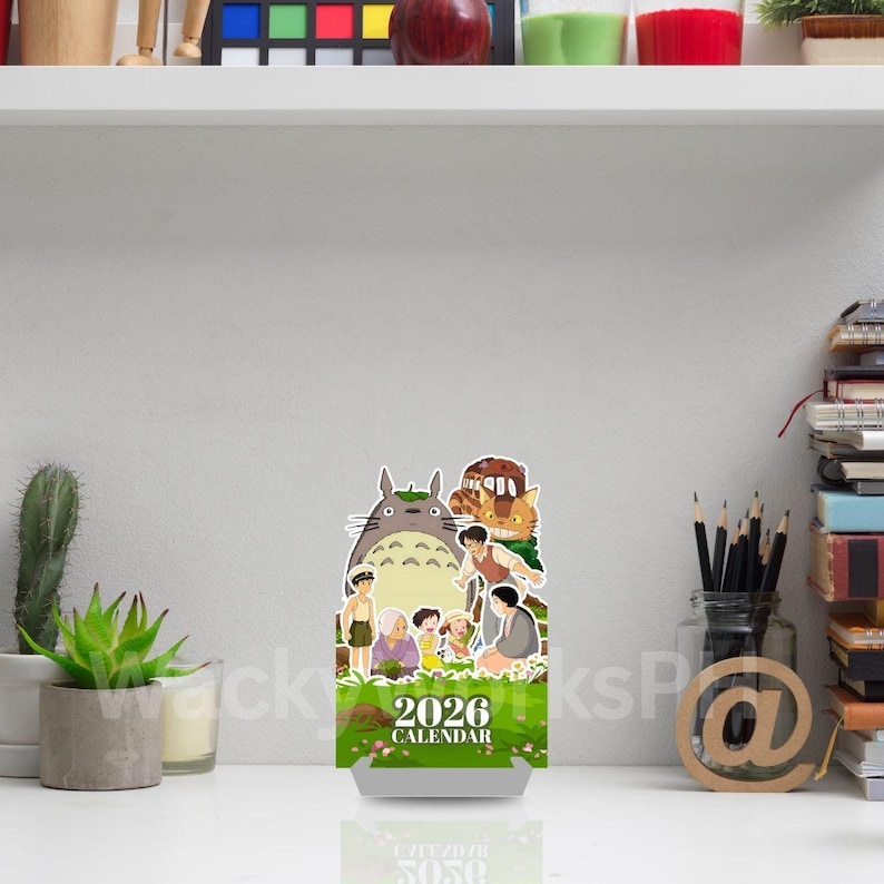 May include: A 2026 calendar featuring a cartoon image of a large, gray Totoro character with other animated characters. The calendar has a green and white base with the text "2026 CALENDAR".