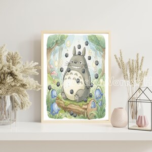 May include: A framed watercolor print featuring a smiling, gray Totoro character surrounded by soot sprites in a forest setting. The artwork includes bluebell flowers, mushrooms, and a log, with a light wood frame.
