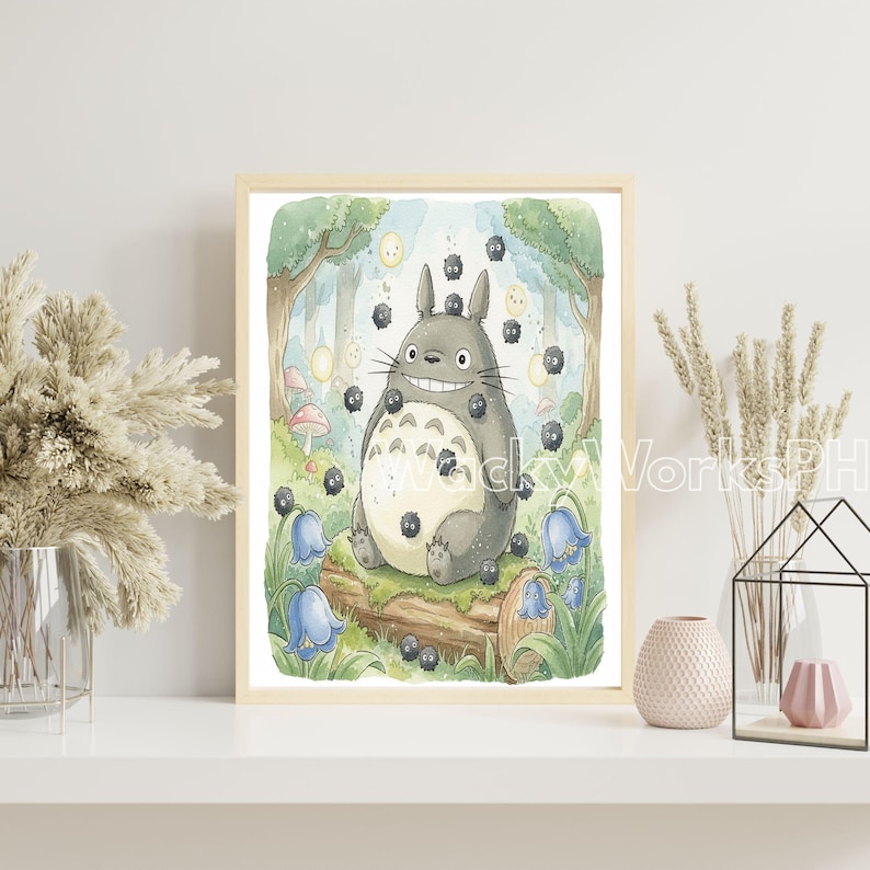 May include: A framed watercolor print featuring a smiling, gray Totoro character surrounded by soot sprites in a forest setting. The artwork includes bluebell flowers, mushrooms, and a log, with a light wood frame.
