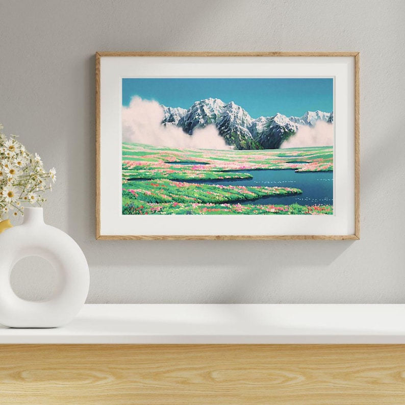 Pu&ograve; includere: Una stampa artistica incorniciata raffigura un paesaggio montano. Vette innevate si ergono su una valle di prati fioriti verdi e rosa e un lago blu. Il cielo &egrave; di un azzurro limpido con soffici nuvole bianche.