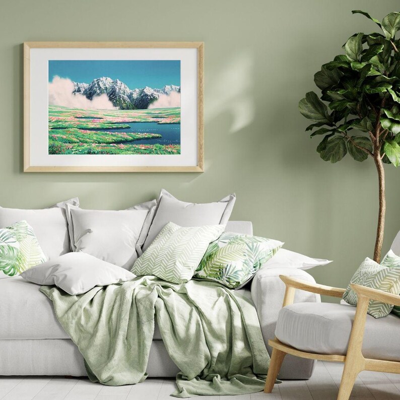 Pu&ograve; includere: Una stampa artistica incorniciata raffigura un paesaggio montano con cime innevate, un lago blu e campi verdi. L'opera d'arte &egrave; esposta sopra un divano bianco con cuscini decorativi e una coperta verde. Una pianta verde &egrave; sullo sfondo.
