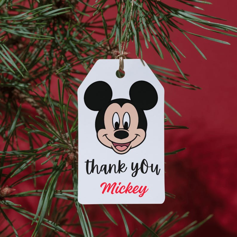May include: A white rectangular gift tag with rounded top corners, featuring a graphic of Mickey Mouse's face at the top. Below the character, the text reads thank you in black script and Mickey in red cursive. A thin gold string hangs from the top hole.