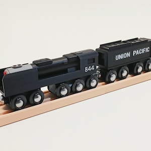 May include: A black wooden toy train with the number "844" on the side and a "UNION PACIFIC" car. The train is on a wooden track. The train has silver wheels and a red light.