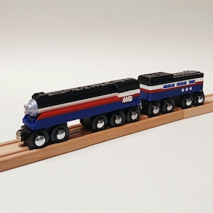 May include: A wooden toy train engine and tender painted in red, white, and blue. The engine features the number 4449 in white, while the tender displays the text American Freedom Train with three white stars. Both pieces have black wheels.