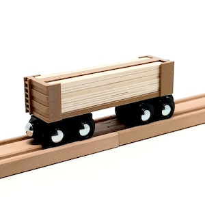 May include: A wooden toy train car with a brown cargo bed filled with wooden planks. The car has four black wheels and is on a brown wooden track.