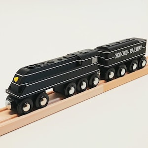 May include: A black wooden toy train with white stripes and silver wheels. The train has a yellow headlight and is on a wooden track. The second car reads "CHOO-CHOO - RAILWAY".