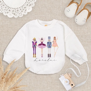 May include: White sweatshirt featuring a colorful illustration of four characters from the Nutcracker ballet. The characters include a king, a ballerina, a soldier, and a dancer. The word "Lorelai" is written in cursive below the characters.