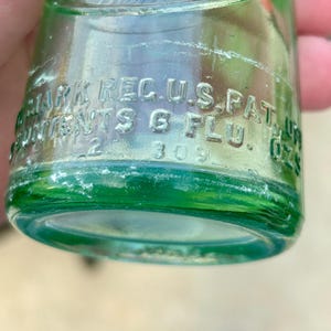 May include: A light green glass bottle with embossed text that reads Drink, Trade Mark Reg. U.S. Pat. Off., and Contents 6 Flu. Ozs. The bottle features a cylindrical base and a curved neck, with the number 309 visible near the bottom edge.