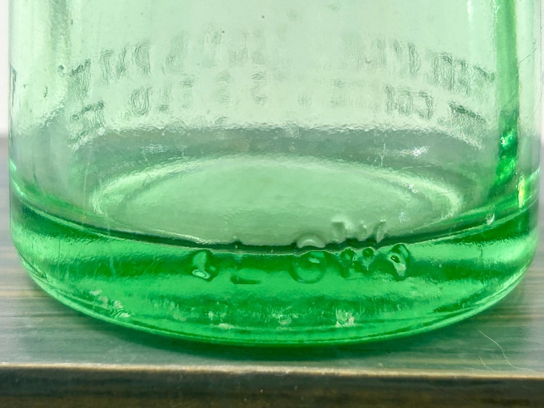 Close-up of an aqua bottle heel and base showing molded letters and small glass bubbles.