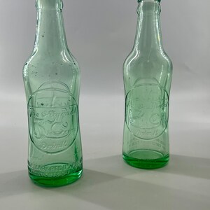 Two bottles shown from front and back to compare embossing and plain glass.