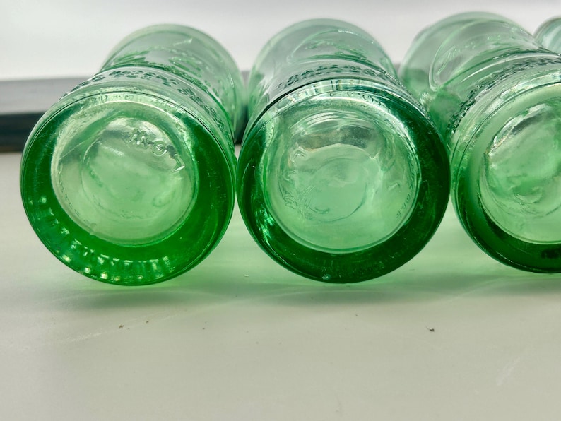 Close bottom views of two bottles with thick aqua glass and circular mold patterns.