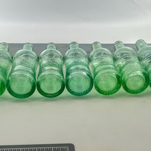 Seven aqua bottle bottoms lined up horizontally to compare base shapes and glass color.