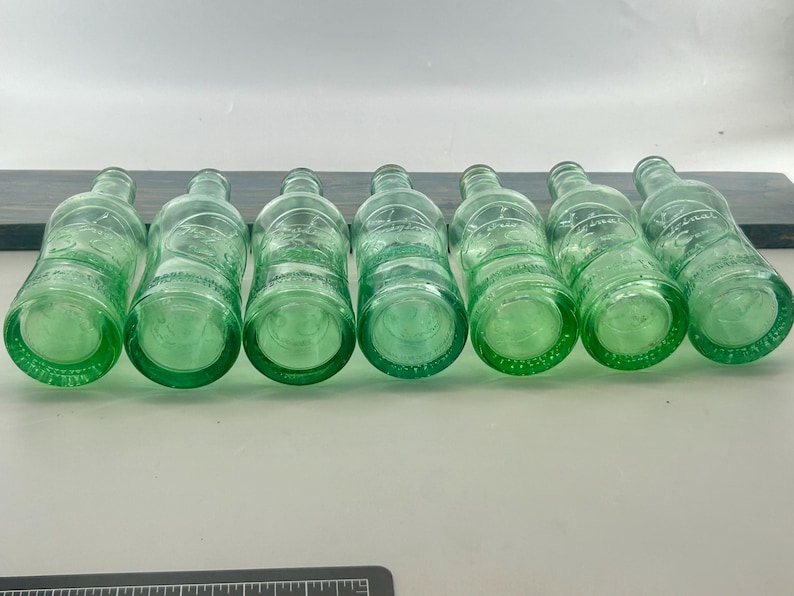 Seven aqua bottle bottoms lined up horizontally to compare base shapes and glass color.