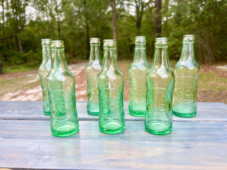 Alternate group view of the seven aqua bottles showing varied shapes and glass tones.
