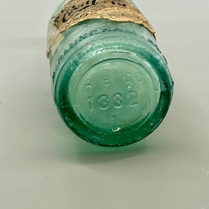 Pode incluir: Uma garrafa de vidro verde claro vintage com um r&oacute;tulo de papel desgastado apresentando o texto Coca-Cola. A base da garrafa &eacute; gravada com as letras A B CO e o n&uacute;mero 1332. O vidro tem um tom de &aacute;gua distinto e fundo arredondado.