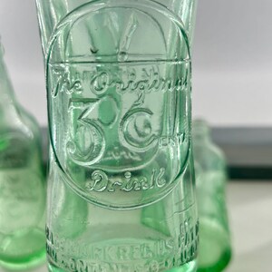 Close-up of raised 3 Centa advertising lettering and decorative embossing on one bottle.