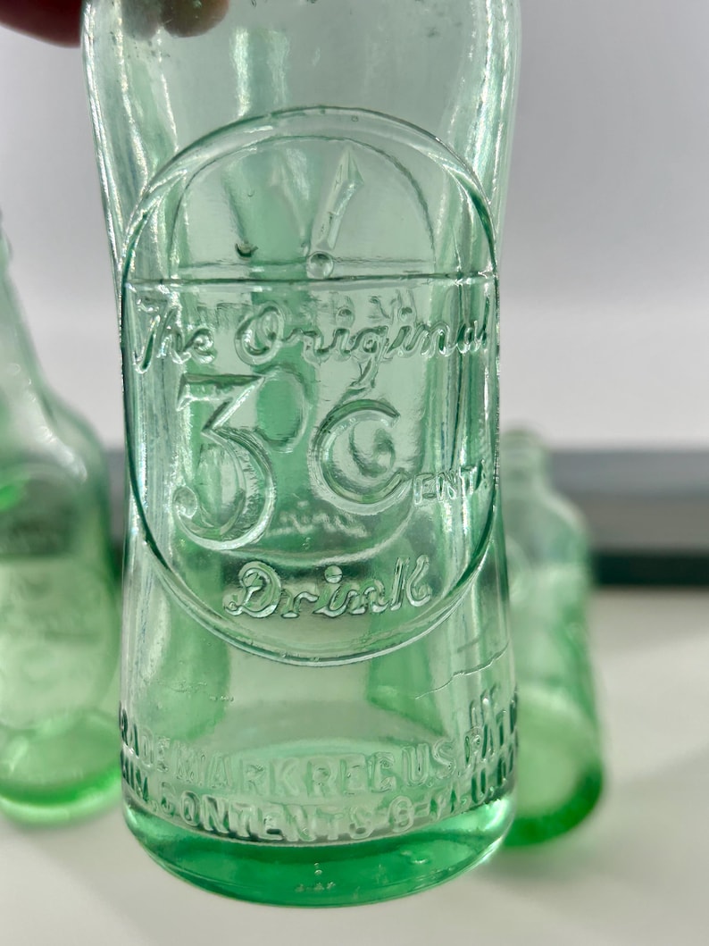 Close-up of raised 3 Centa advertising lettering and decorative embossing on one bottle.