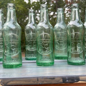 Front group view of several embossed 3 Centa bottles lined up outdoors.