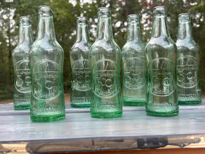 Front group view of several embossed 3 Centa bottles lined up outdoors.
