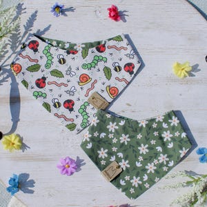 May include: Two pet bandanas. One is white with a pattern of bugs, including ladybirds, bees, and caterpillars. The other is green with a white floral pattern. Both have a tag that says "Magnolia".