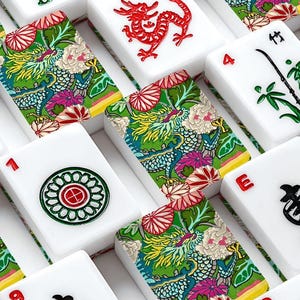 May include: A close-up of a Mahjong set with white tiles. The tiles display numbers, symbols, and Chinese characters in red and black. Some tiles have a colourful floral and dragon design.