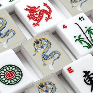 May include: A collection of rectangular mahjong tiles featuring various designs including a red dragon, a blue and yellow dragon, green bamboo stalks, a circular floral pattern, and the letter E, all set against a white or light gray background.