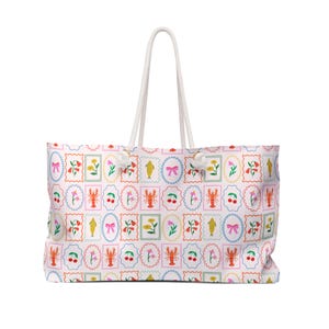 May include: A large tote bag with a white background and a repeating pattern of colourful postage stamp-like designs. The stamps feature images of lobsters, cherries, flowers, and bows. The bag has white rope handles.