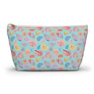 May include: A cosmetic bag with a zip closure, featuring a light blue backdrop and a repeating pattern of colourful seashells. The seashells are in shades of pink, yellow, orange, and blue. The zip is gold.