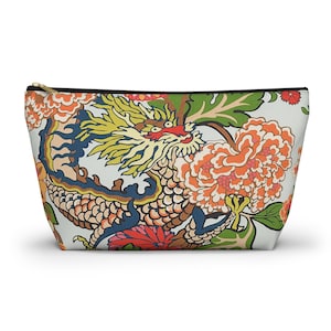 May include: A zippered cosmetic bag featuring a colorful dragon design. The dragon is depicted with yellow, red, and blue details, surrounded by orange and red flowers and green foliage. The bag has a black zipper and a light background.