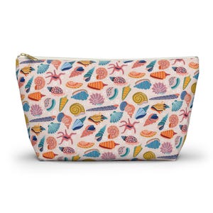 May include: A zipped pouch featuring a pattern of colourful seashells, starfish, and marine life on a pale pink backdrop. The design incorporates orange, blue, yellow, and purple elements. The pouch has a gold-coloured zip.