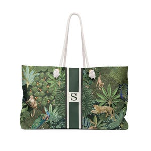 Könnte beinhalten: Große Tragetasche mit Dschungel-Print. Die Tasche hat einen grün-weißen Streifen mit dem Buchstaben "S" in der Mitte. Die Dschungelszene zeigt Affen, einen Leoparden und einen Pfau. Weiße Seilgriffe runden das Design ab.