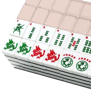 May include: A close-up of a Mahjong set with white tiles. The tiles feature red and green dragon designs, along with numbers and symbols. The set includes a clear plastic case for storage.