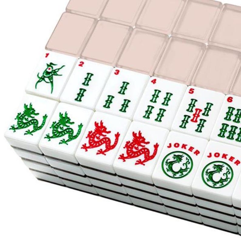 May include: A close-up of a Mahjong set with white tiles. The tiles feature red and green dragon designs, along with numbers and symbols. The set includes a clear plastic case for storage.