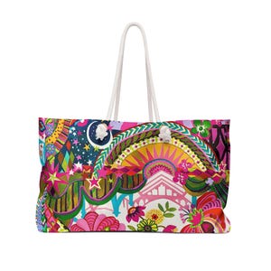 May include: A large tote bag featuring a vibrant, multi-colored graphic print with stars, a crescent moon, floral motifs, and geometric patterns in shades of pink, yellow, green, and blue. The bag includes two white rope handles attached at the top.