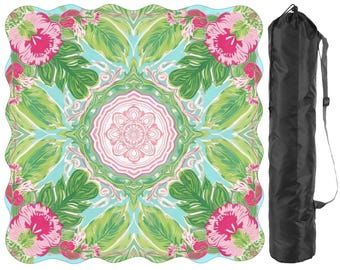 May include: A colorful yoga mat with a floral design featuring pink flowers and green leaves on a light blue background. The mat has a scalloped edge and comes with a black carrying bag with a shoulder strap.