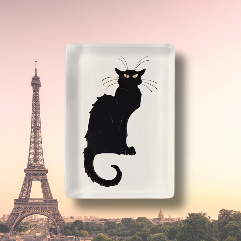 May include: A rectangular white ceramic tray featuring a centered illustration of a black cat with arched back, long whiskers, and yellow eyes. The cat is depicted in a seated position with its tail curled at the base of the tray.