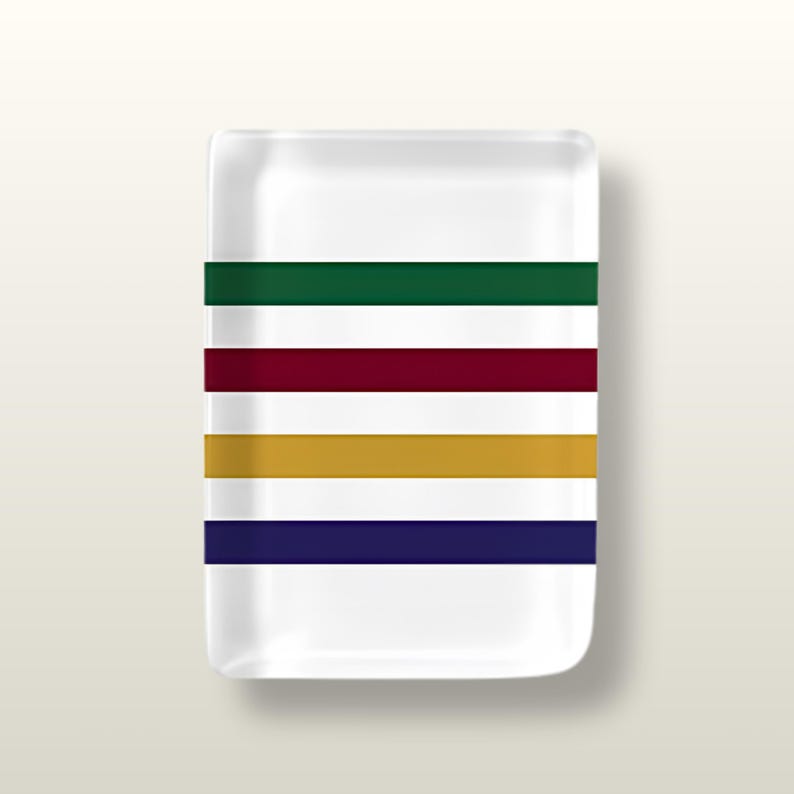 May include: A rectangular white ceramic tray featuring four horizontal stripes in dark green, deep burgundy, mustard yellow, and navy blue. The tray has rounded corners and a smooth, glossy finish, providing a clean surface for small items.