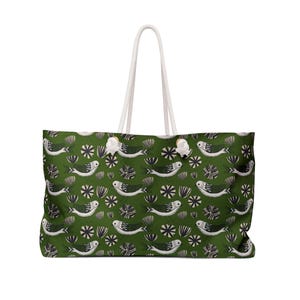 Peut inclure: Grand sac fourre-tout avec un motif répété de poissons stylisés et d'éléments floraux blancs, noirs et vert foncé sur fond vert. Le sac a des poignées en corde blanche.