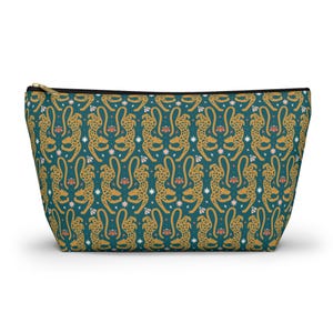 Peut inclure: Une trousse zippée turquoise avec un motif répété de guépards dorés, de fleurs roses et d'étoiles blanches. La trousse a une fermeture éclair noire et une doublure noire. Le sac est conçu pour contenir des cosmétiques ou d'autres petits objets.