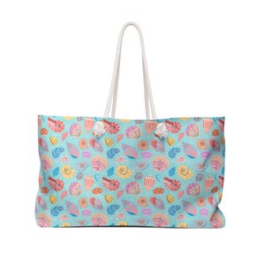 May include: A large tote bag featuring a pattern of colourful seashells on a light blue background. The bag has white rope handles. The seashells are in shades of pink, yellow, orange, and blue.