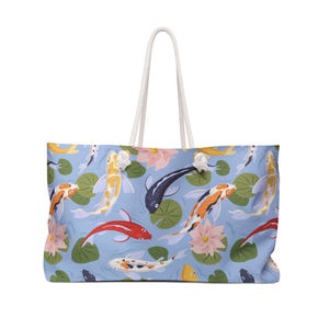 May include: Large tote bag with a light blue background featuring a pattern of koi fish, lily pads, and lotus flowers. The koi fish are in various colors, including orange, yellow, red, and black. The bag has white rope handles.