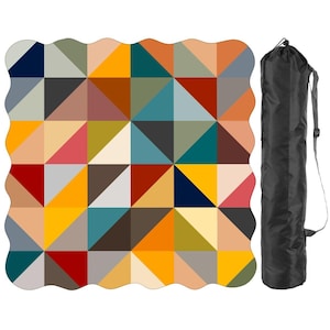 May include: A square picnic blanket with scalloped edges featuring a geometric pattern of multicolored triangles in shades of navy, yellow, teal, red, orange, gray, and beige, accompanied by a black cylindrical carrying bag with a shoulder strap.