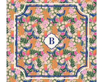 Puede incluir: Una alfombrilla decorativa cuadrada con un denso patrón floral de flores rosas, naranjas y blancas sobre un fondo verde salvia. Un borde festoneado azul oscuro y blanco enmarca el centro, que contiene un emblema blanco con la letra B.