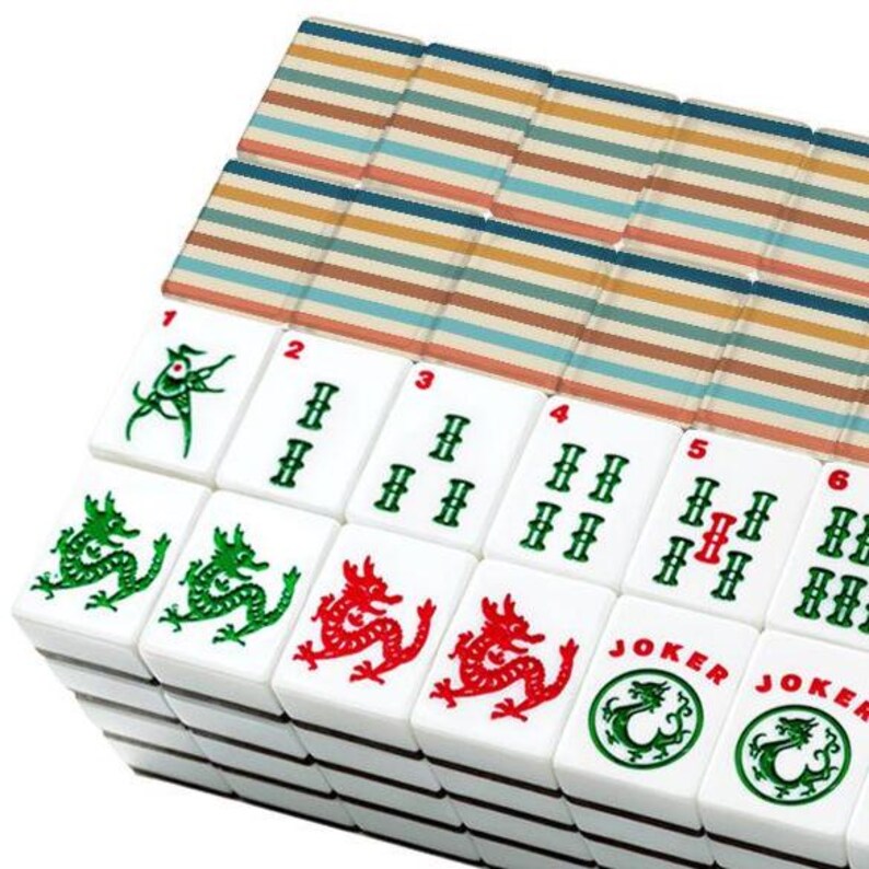 Pode incluir: Um conjunto de pe&ccedil;as retangulares de mahjong dispostas em filas. As faces frontais apresentam ilustra&ccedil;&otilde;es de drag&otilde;es verdes e vermelhos, naipes de bambu numerados e pe&ccedil;as Joker circulares. Os versos exibem um padr&atilde;o de listras horizontais.