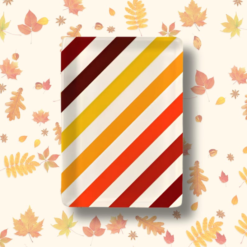 Op de afbeelding: Een rechthoekig dienblad met een herhalend diagonaal streeppatroon in tinten donker kastanjebruin, felgeel, oranje en rood. Het dienblad heeft een gladde, glanzende afwerking en strakke, rechte randen, wat zorgt voor een levendig geometrisch ontwerp.