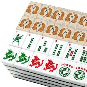 May include: A set of white mahjong tiles arranged in rows. The top row features translucent tiles with a leopard pattern and the letter S. The lower rows display white tiles with green and red ink illustrations of dragons, numbers 1 through 6, and Joker tiles.