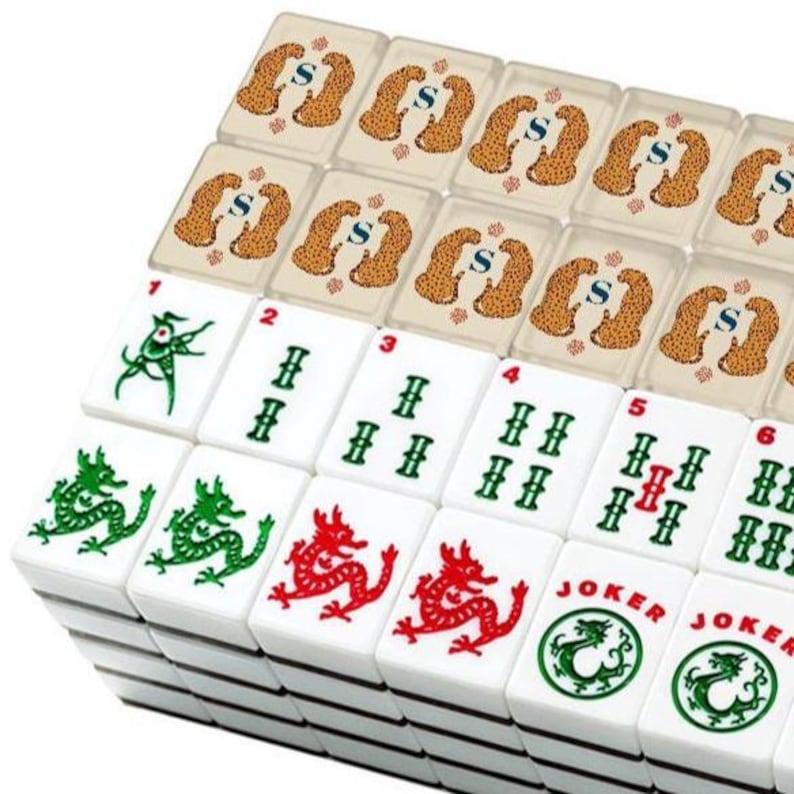 May include: A set of white mahjong tiles arranged in rows. The top row features translucent tiles with a leopard pattern and the letter S. The lower rows display white tiles with green and red ink illustrations of dragons, numbers 1 through 6, and Joker tiles.